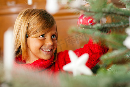 小女孩帮忙装饰圣诞树，手里拿着一些圣诞小玩意儿(关注女孩)
