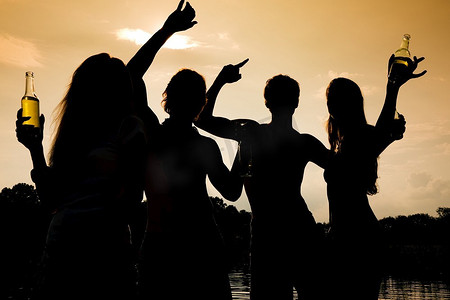 朋友聚会剪影摄影照片_海滩上的人们(两对)随着音乐跳舞，喝酒，在夕阳下只能看到的人群的剪影中玩得很开心