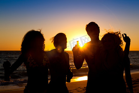 人们(两对夫妇)在海滩上举行派对,在夕阳下喝酒,玩得很开心(只有剪影