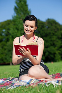 夏天坐在草地上的女人在阳光下看书