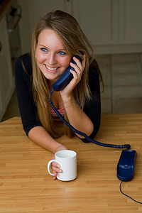 一个年轻漂亮的女人在电话里愉快地聊天，喝着一杯茶/咖啡