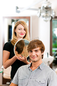 男士发型摄影照片_理发师的男士，她剪完了头发，正在镜子里展示发型。