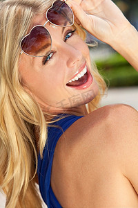 美丽快乐的年轻金发女子笑着，戴着心形太阳镜