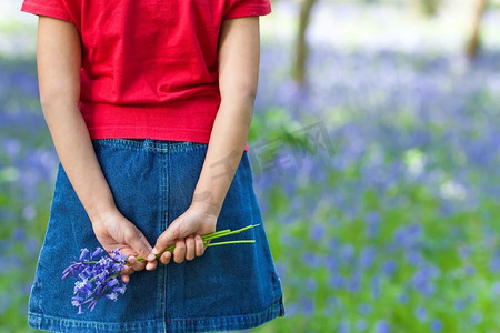 拍摄的是一个小女孩背着一堆蓝色的铃铛，背景是一片蓝铃木，背景模糊。