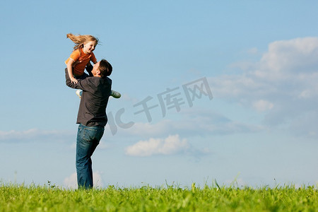 父亲和他的儿女一起在草地上玩耍，在一个夏末的下午，他把女儿抛向空中，这是家庭的概念