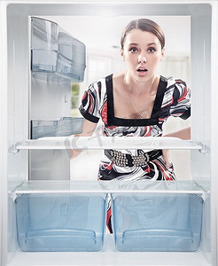 冰箱里的水果摄影照片_年轻女子看着冰箱里空着的货架。