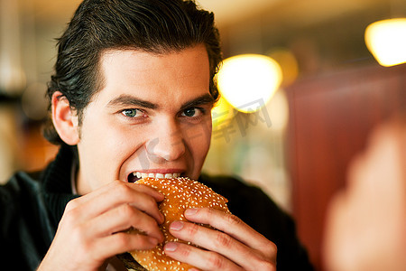 在餐馆或餐馆里吃汉堡包的人，他饿了，用可用光线拍摄，非常有选择性地吃了一口