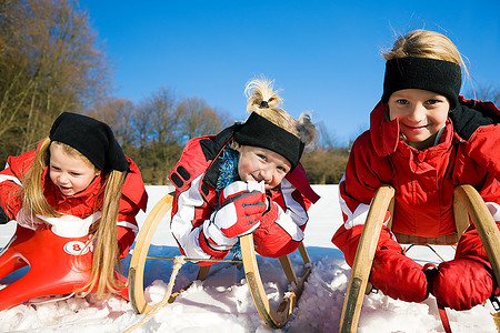 三个小孩在雪地里的山顶上拉着雪橇，等着开始玩这个游戏。
