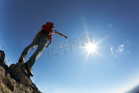登山者穿着登山装备，站在他路线顶端的一块石头上，越过了深蓝色的天空。