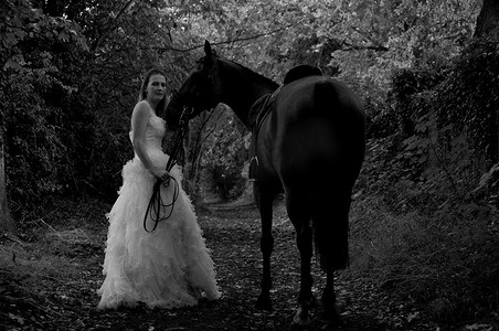 育成摄影照片_穿着婚纱的女人骑在马上。