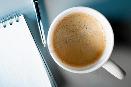 一杯咖啡和笔记本在桌子上在蓝色的光。专注于马克杯