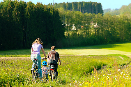 一家人带着自行车去旅行，风景很美，因为他们的儿子太小了，他正在骑一辆训练自行车