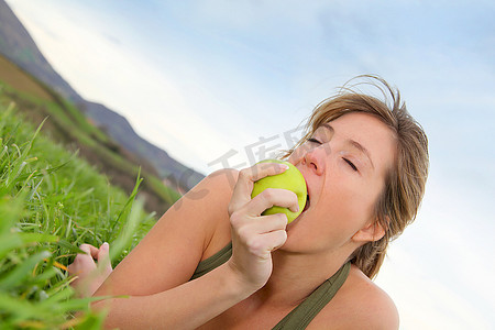 美丽的女人在大自然中吃着青苹果