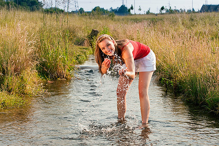 一名妇女站在一条小溪里，脚踝浸入水中，凉水在夏日的炎热中令人耳目一新