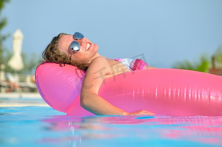 一个年轻的女人在游泳池里的粉红色空气床