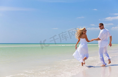 牵手奔跑摄影照片_一对幸福的年轻男女在蔚蓝天空的荒凉热带海滩上奔跑、欢笑、牵手