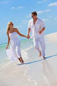 牵手奔跑摄影照片_一对幸福的年轻男女在蔚蓝天空的荒凉热带海滩上奔跑、欢笑、牵手