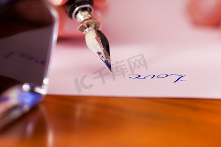 一个女人(只有一只手被看到)用钢笔和墨水在纸上写字，前景中她有一个墨水罐