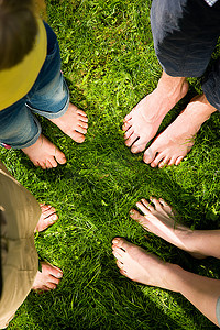 足科摄影照片_健康足系列：不同年龄的男性和女性的脚在草丛中站成一个圆圈，手持雏菊，从上面看