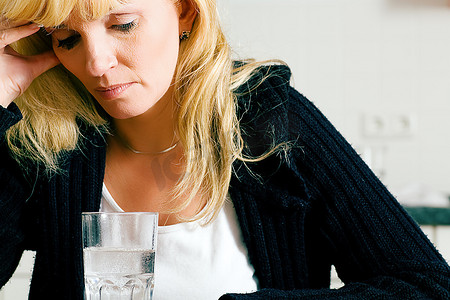 偏头痛摄影照片_有严重宿醉或偏头痛的妇女拿着止痛药坐在一杯水前
