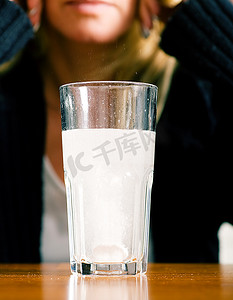 有严重宿醉或偏头痛的妇女拿着止痛药坐在一杯水前