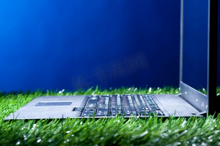 草地上的现代笔记本电脑在黑暗中照亮，侧视