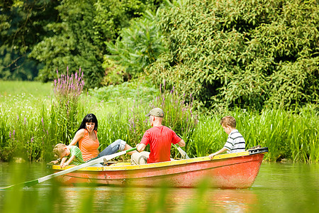 一家人带着两个孩子在湖上划船旅行，背景是许多树木和鲜花