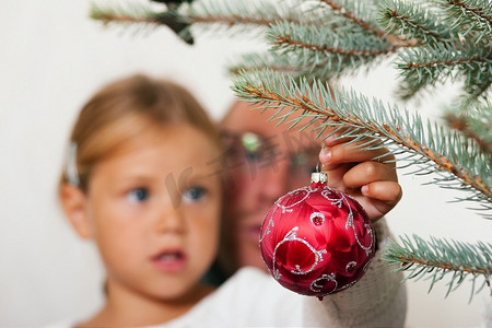 小女孩帮父亲装饰圣诞树，手里拿着一些圣诞小玩意儿(重点放在小玩意儿上！)