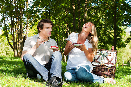 坐在草地摄影照片_夫妇坐在草地在夏天有一个野餐与草莓蛋糕
