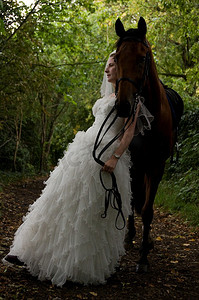 穿婚纱的女人靠在马背上。