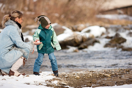 一家人--母亲和儿子--冬天沿着河岸散步；孩子在扔雪球