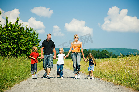 阳光明媚的夏日，幸福的一家人走在一条小路上