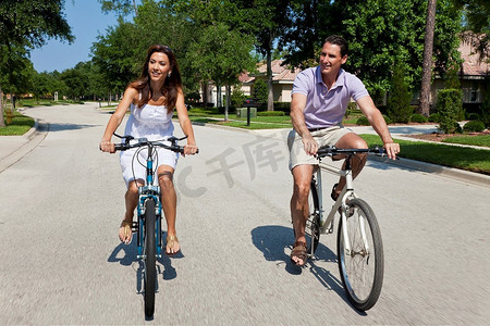 骑情侣摄影照片_两个迷人的成年人，男女情侣，一起骑自行车，用缓慢的快门速度和运动模糊拍摄的。