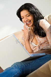 一位年轻漂亮的西班牙裔妇女一边用笔记本电脑一边笑着
