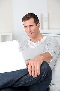 拿着电脑的男人摄影照片_成年男子坐在沙发上拿着笔记本电脑的特写