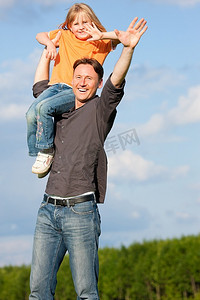 父亲和他的儿女一起在草地上玩耍，他把她扛在肩上