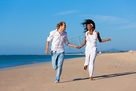 一对夫妇--黑人女性和高加索男性--在假期中沿着海滩散步和跑步