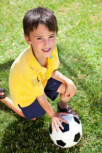 一个小男孩在外面踢足球，跪在球门阴影下的草地上
