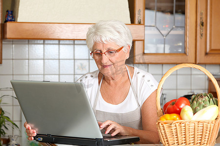 厨房里拿着笔记本电脑的老年妇女
