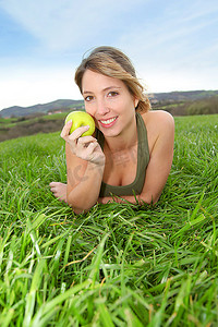 美丽的女人在大自然中吃着青苹果