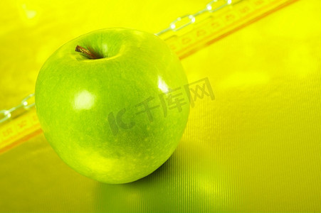 绿色的苹果放在金色的背景上，上面有卷尺和链子