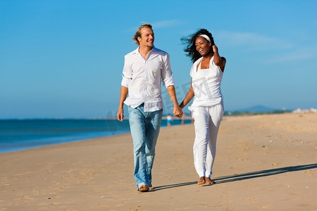 一对幸福的夫妇--黑人女性和高加索男性--在假期中沿着海滩散步和跑步