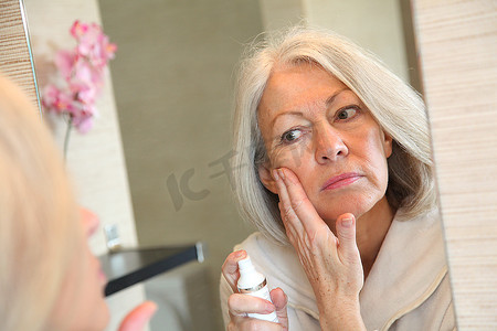 老年妇女在脸上涂抹保湿霜