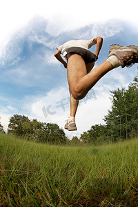 下云朵摄影照片_男性跑步者在蓝天和云朵的映衬下在草地上跳跃和奔跑；模糊效果，鱼眼镜头。复制-底部的空格。