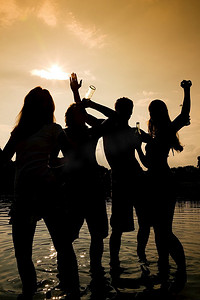 海滩上的人们(两对)随着音乐跳舞，喝酒，在夕阳下只能看到的人群的剪影中玩得很开心