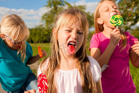三个女孩在吃棒棒糖，前面的女孩伸出舌头