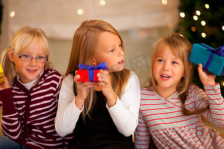 圣诞树前的三个女孩带着礼物