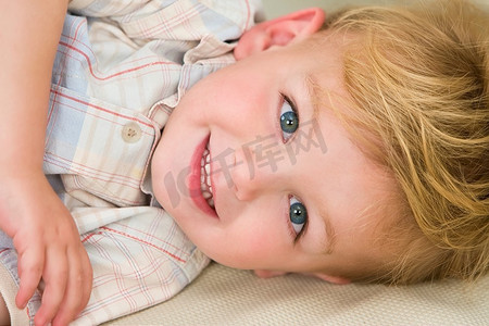 厚颜无耻摄影照片_一个年轻的金发男孩穿着，躺着，露出厚颜无耻的笑容