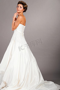 美丽的新娘穿着婚纱站在灰色的背景上，侧视