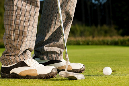 洞阳光摄影照片_高尔夫球手将球打入洞内，只能看到脚和铁头
